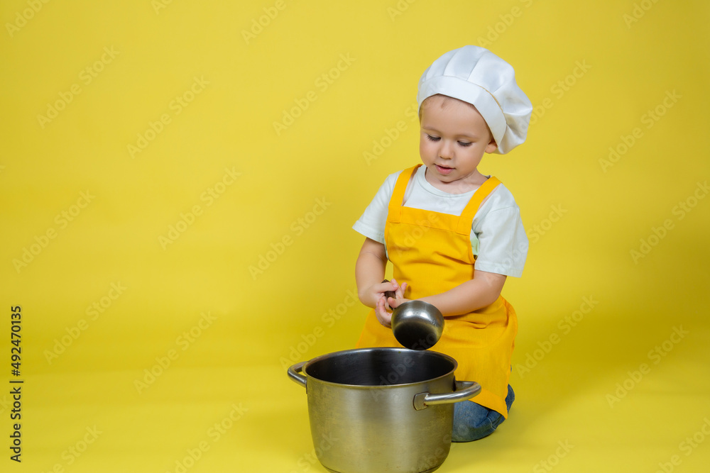Boy in apron and chef's hat sitting on the floor with a saucepan and ladle Boy in apron and chef's hat sitting on the floor with a saucepan and ladle