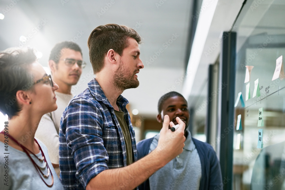 Hes making sure his plans are heard. Shot of a group of designers brainstorming with notes on a glass wall in an office. Hes making sure his plans are heard. Shot of a group of designers brainstorming with notes on a glass wall in an office.