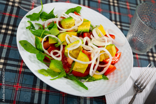 Colorful salad with fresh ripe tomatoes, green ripe avocado, sliced onion and herbs. Vegetarian appetizer