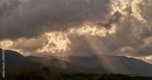 Bright sunlight shining through hole of clouds to dark scene of mountain range before sunset valley