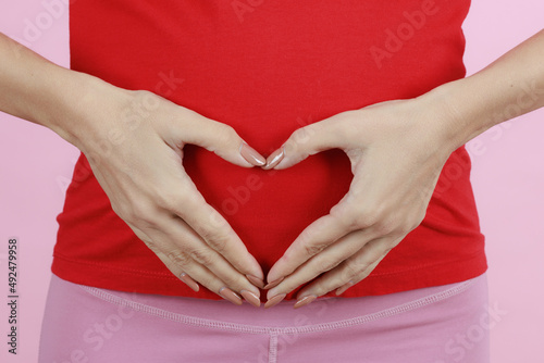 Hands of a mother putting on belly in heart sign or symbol. Concept of love, care and woman awaiting for coming newborn baby. Close-up shot