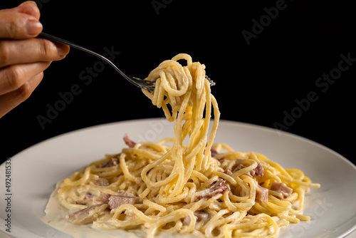 fork is spinning carbonara spaghetti on white plate on black background