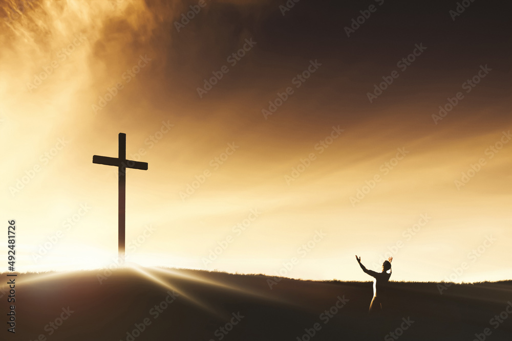 하늘과 구름 사이로 빛나는 예수그리스도의 거룩한 십자가를 향해 두 손을 들고 기도와 찬양과 경배하는 사람
