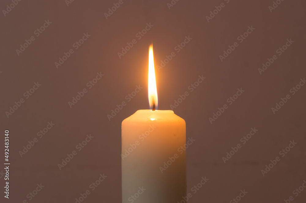 A single burning candle flame isolated on black or dark background on table in church for Christmas, funeral and memorial service A single burning candle flame isolated on black or dark background on table in church for Christmas, funeral and memorial service