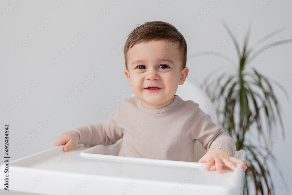 cheerful smiling baby is sitting in a white high chair for feeding. white background