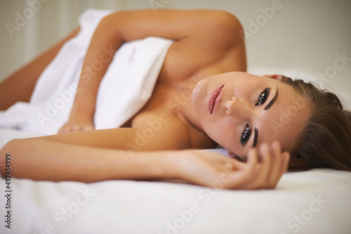 Tempted to stay in bed all day. An attractive woman lying in bed with only a sheet to cover her.