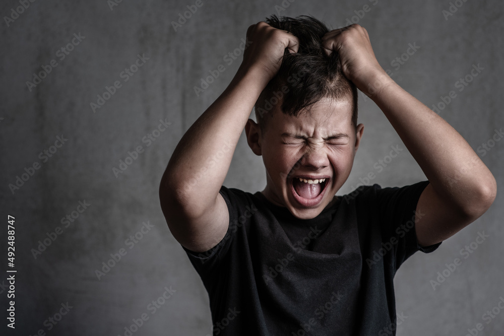 Teen boy screaming in anger on dark background Teen boy screaming in anger on dark background