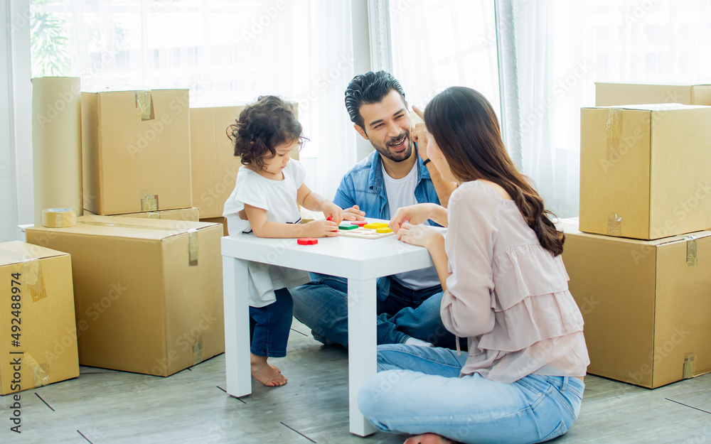 Caucasian handsome father, asian beautiful mother, little mixed race adorable girl or daughter sitting on floor, family playing together with happiness, moving house or apartment with paper boxes. Caucasian handsome father, asian beautiful mother, little mixed race adorable girl or daughter sitting on floor, family playing together with happiness, moving house or apartment with paper boxes.