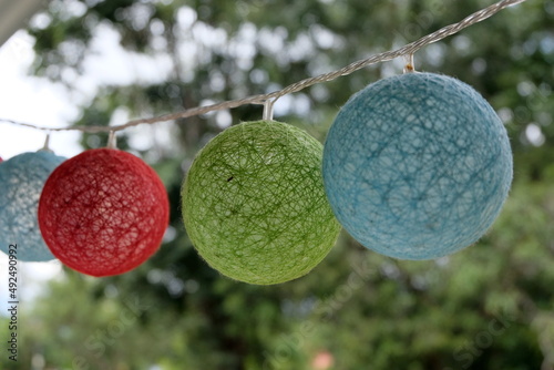 Cool colourful blue, green and red round textured bubble bauble lights hanging outdoors during a celebration with trees in background