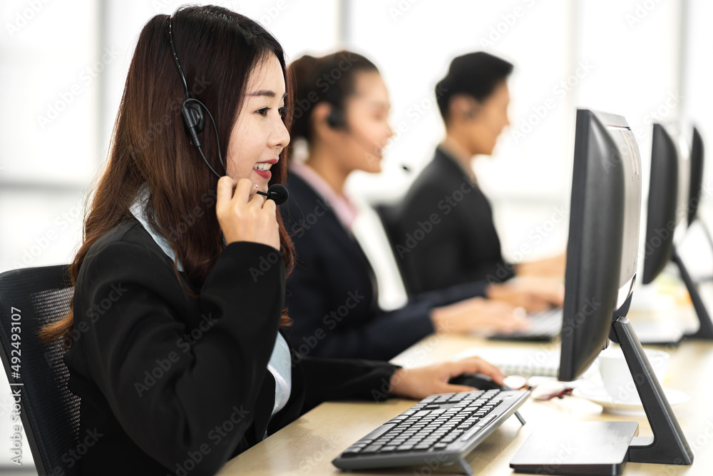 Group of happy call center smiling asian business operator customer help support team phone services agen working and talking with headset on desktop computer at call center office Group of happy call center smiling asian business operator customer help support team phone services agen working and talking with headset on desktop computer at call center office