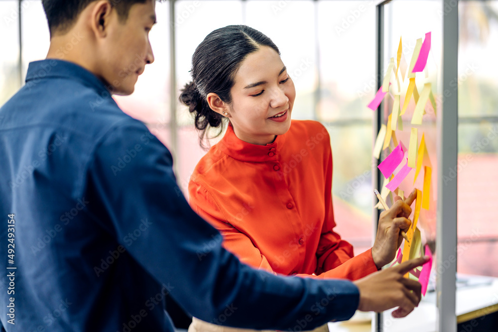 Casual creative happy two smile asian business people plan strategy analysis and brainstorm putting post it sticker note to share idea for startup project on glass board at modern office