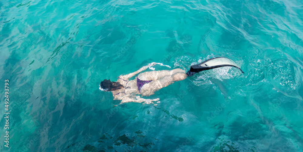 Beautiful sport woman wearing swimming suite under free diver glides over sandy sea with scuba and fins. Woman free diver in summer holiday.