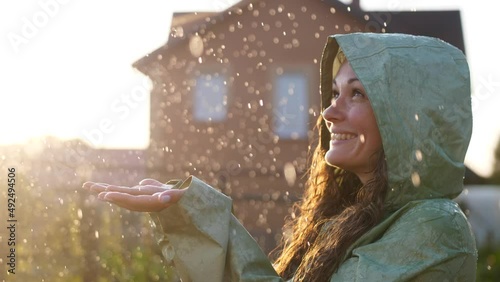 Young happy woman wearing raincoat is feeling free and smiling under the rain. Concept of life, freedom, nature, adventure, purity.