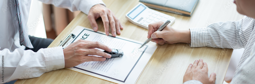 Insurance concept the customer signing his name on the contract while the dealer giving more details Insurance concept the customer signing his name on the contract while the dealer giving more details