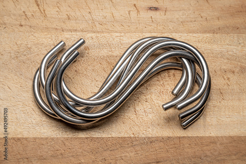 A group of Stainless Steel Hooks isolated on a wooden background. Hand ground and polished ready to hang.