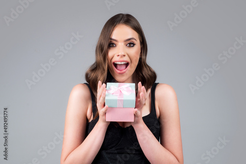 Excited woman with present gift box posing with surprised face expression, isolated background. Christmas, valentines or birthday gifts. Beauty portrait of beautiful female model.