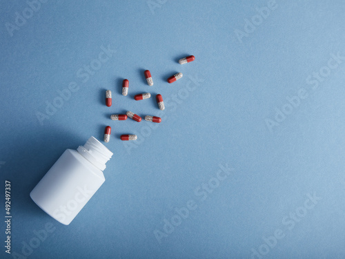 Capsules falling from the white bottle on blue paper background. Concept of pharmacy.