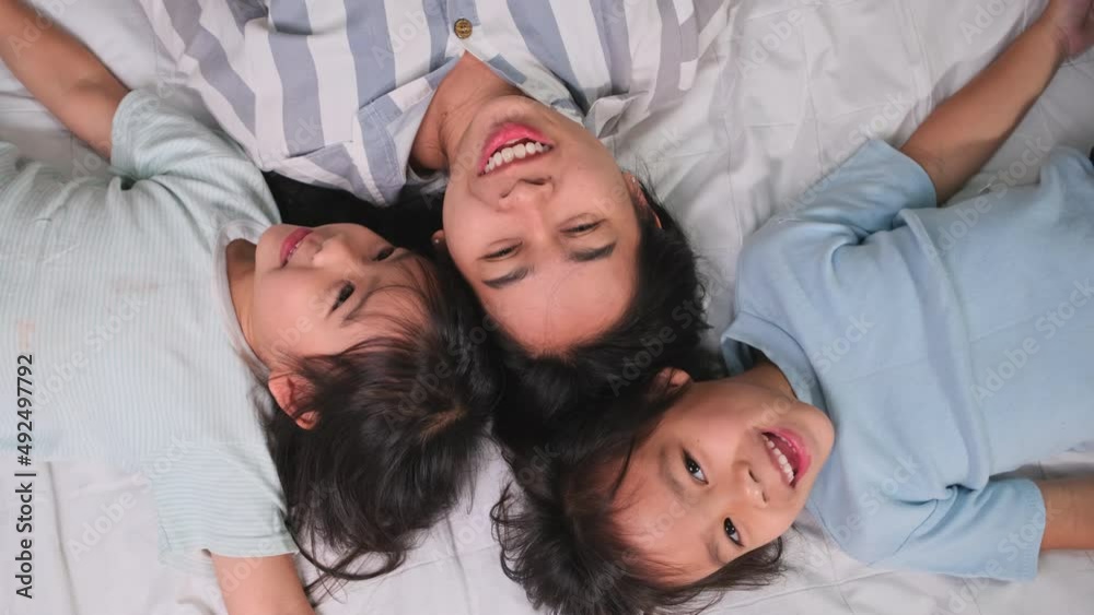 Top view portrait of Happy children playing with their mother lying on a bed at home. Good time at home. Concept of parenting and family happiness.