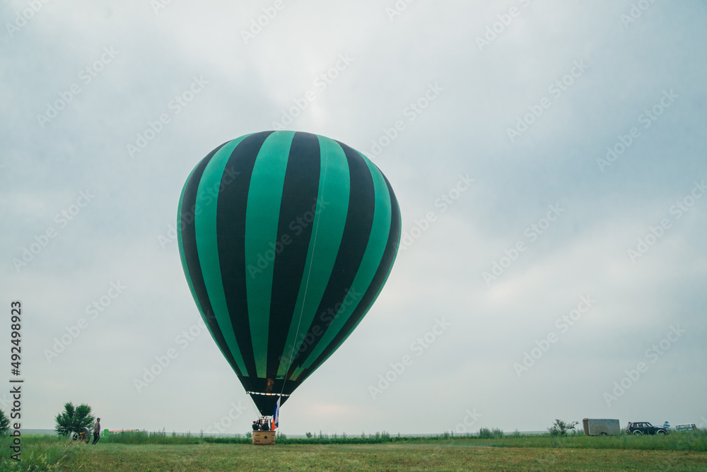 Obraz premium Inflating, unpack and flying up hot air balloon watermelon. Burner directing flame into envelope. Take off aircraft fly in morning blue sky. Start hot air burning to inflate gas fire to air balloon.