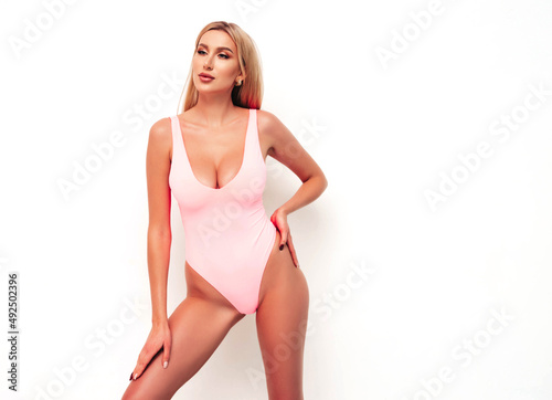 High fashion portrait of young beautiful sexy woman. Carefree model wearing pure pink lingerie with big breasts. Hot tanned blonde posing near wall in studio in summer swimwear bathing suit