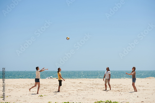 Group of happy young people ing volleyball on beach on sunny day