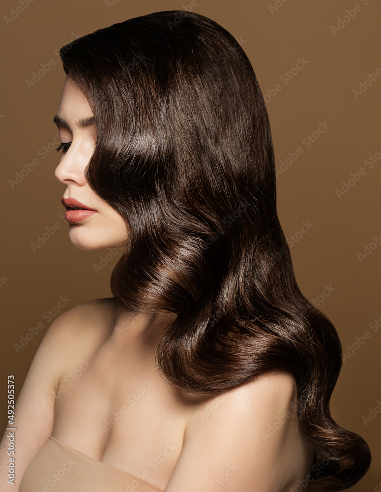 Model Waves Hairstyle. Brunette Beauty with Smooth Hollywood Curls. Woman with Shiny Wavy Hair and Nude Make up over Beige Background Model Waves Hairstyle. Brunette Beauty with Smooth Hollywood Curls. Woman with Shiny Wavy Hair and Nude Make up over Beige Background