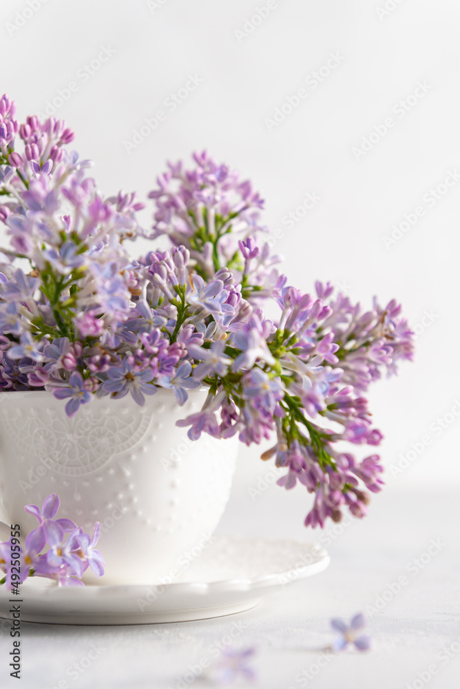 Romantic spring background with branches of blooming lilac in a tea cup on a white background. Tender floral greeting card, poster, invitation, background. Close up. Floral shop