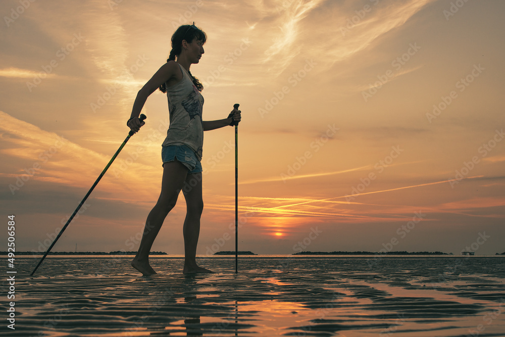 Girl practicing Nordic walking on the beach at dawn