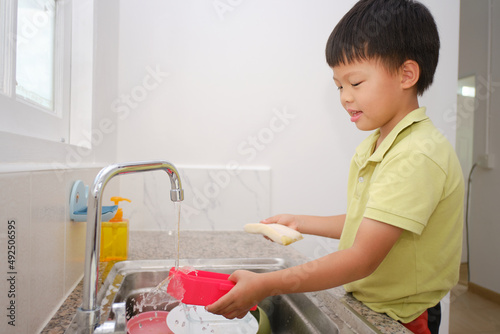 Fotografie Cute little Asian kindergarten boy child doing the dishes, washing dishes in kit