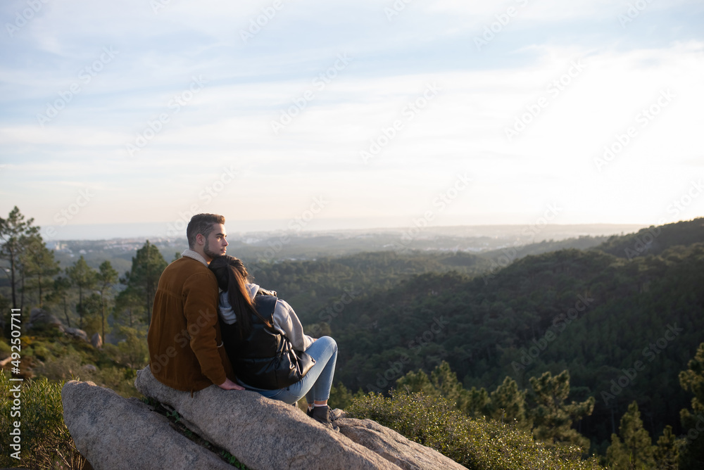 Tender couple resting after hiking in autumn. Man and woman in casual clothes with hiking ammunition sitting at peak, leaning on shoulder. Nature, activity, hobby concept Tender couple resting after hiking in autumn. Man and woman in casual clothes with hiking ammunition sitting at peak, leaning on shoulder. Nature, activity, hobby concept