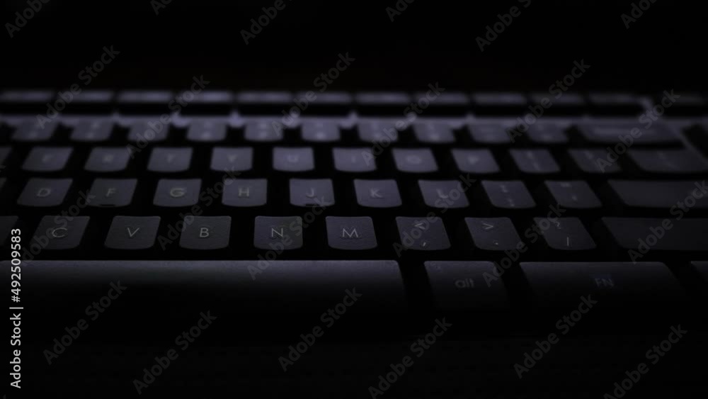 Panning shot of a keyboard lit by a computer screen. Panning shot of a keyboard lit by a computer screen.