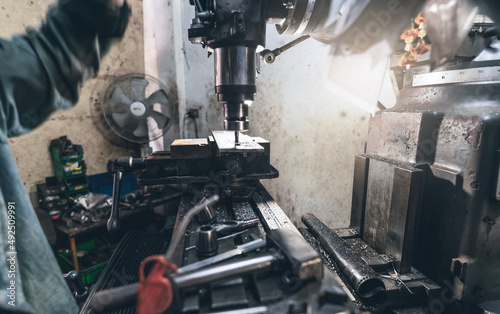 Selective focus on milling machine. Blurred worker is working on milling machine to milling metal plate. Tool for cut metal workpiece. Steel manufacturing factory. Milling process. Machine in workshop