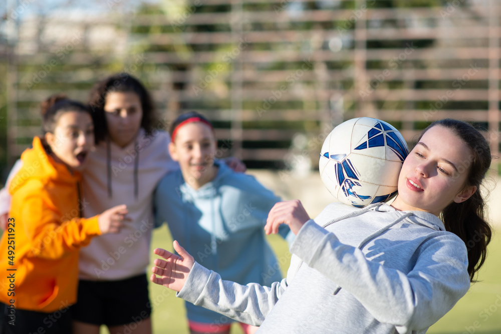 Fototapeta premium Happy school girls having fun with ball on stadium. Team of four joyous girlfriends preparing for football game training to win and demonstrating skills. Healthy lifestyle, leisure, team sport concept