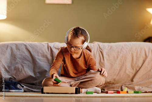 Portrait of young girl with down syndrome playing with toy blocks alone and wearing noise cancelling earphones, overstimulation concept, copy space photo