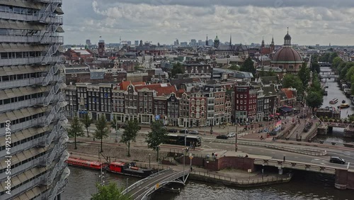Amsterdam Netherlands Aerial v20 pull out shot away from rows of dutch townhouses at prins hendrikkade street, reveal central station railroad tracks and river cruise docked at terminal - August 2021 photo