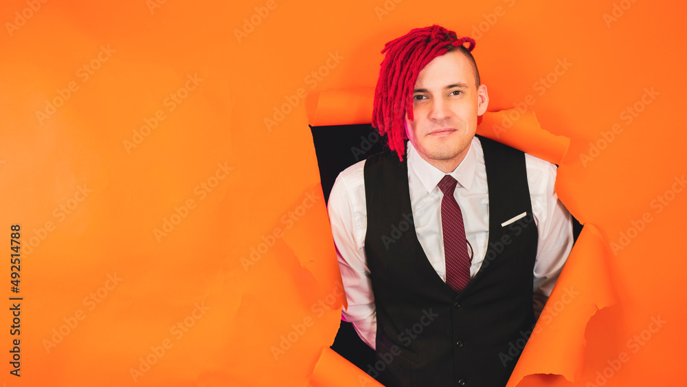 Smiling man with red dreadlocks in hole in wall. Stylish male with bright dreadlocks looking at camera through hole in orange wall in studio Smiling man with red dreadlocks in hole in wall. Stylish male with bright dreadlocks looking at camera through hole in orange wall in studio