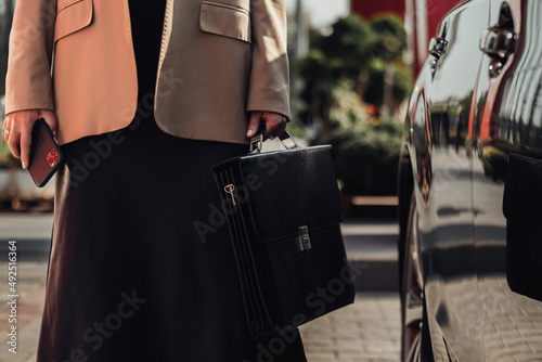 Unrecognisable Elegant Business Woman with Briefcase and Smartphone Standing Near the Luxury Car