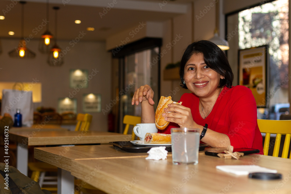 Happy latina woman having breakfast in a cafe having a sandwich and coffee. Happy latina woman having breakfast in a cafe having a sandwich and coffee.