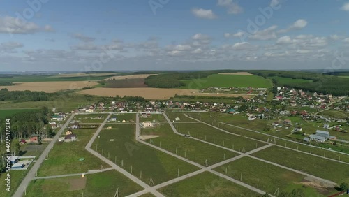 Aerial view of construction houses in new residential area. There are many vacant land plots. Dirt roads in the village, houses and electric poles are being built. Around the meadows, fields and fores