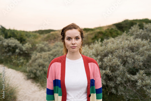 Beautiful young woman wearing multi colored cardigan sweater standing in meadow photo