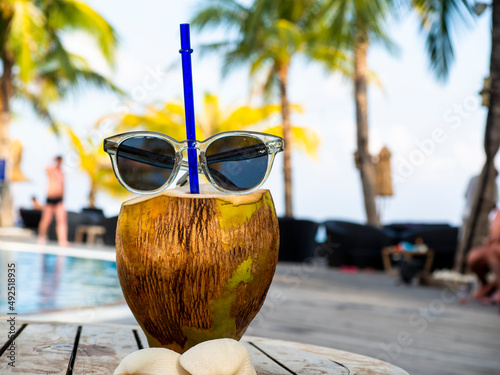 Sunglasses on top of cracked coconut with drinking straw inside photo
