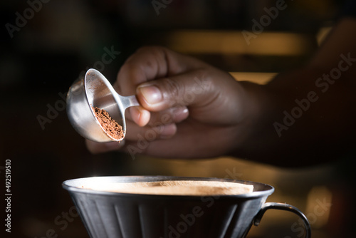 filling grinded coffee beans in paper filter cone by metal spoon with dark yellow background