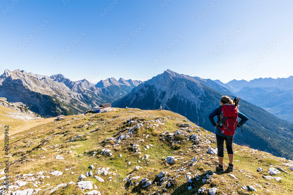 Female hiker admiring surrounding landscape from mountaintop withTiroler Hutte retreat in background Female hiker admiring surrounding landscape from mountaintop withTiroler Hutte retreat in background