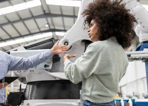 Developer discussing with colleague about robotic arm in factory photo