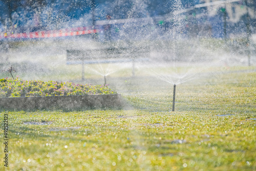 Automatic garden lawn sprinkler in action on a growing public garden during a spring beautiful day.