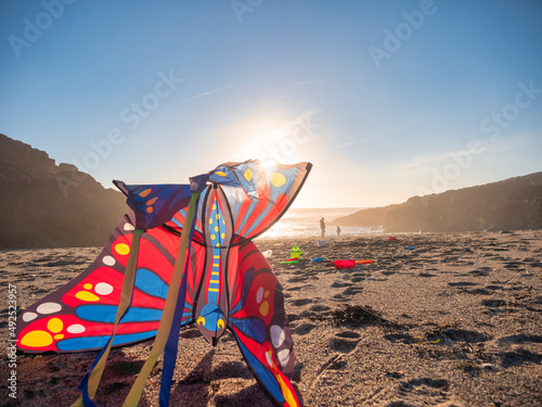 Sun setting behind butterfly shaped kite lying on sandy beach