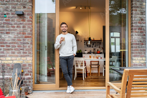 Smiling man with glass of coffee leaning on doorway photo
