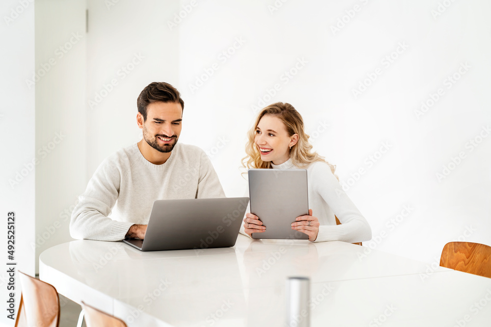 Smiling blond woman with tablet PC looking at colleague using laptop Smiling blond woman with tablet PC looking at colleague using laptop