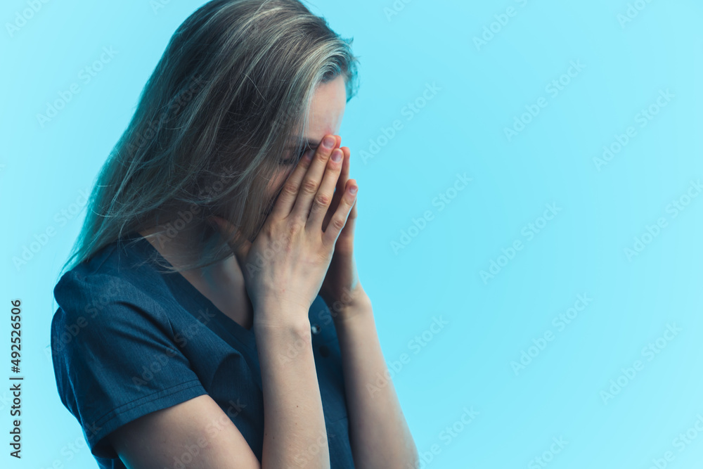 Exhausted caucasian woman in her 30s covering her face with two palms over blue background. Studio shot. High quality photo Exhausted caucasian woman in her 30s covering her face with two palms over blue background. Studio shot. High quality photo