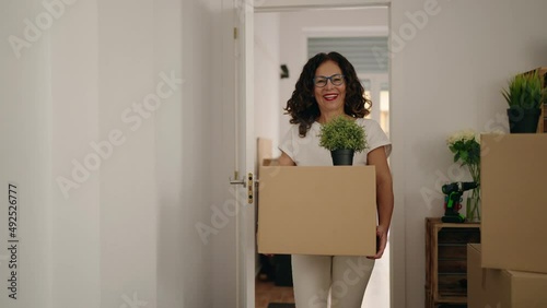 Middle age woman smiling confident holding package walking at new home photo